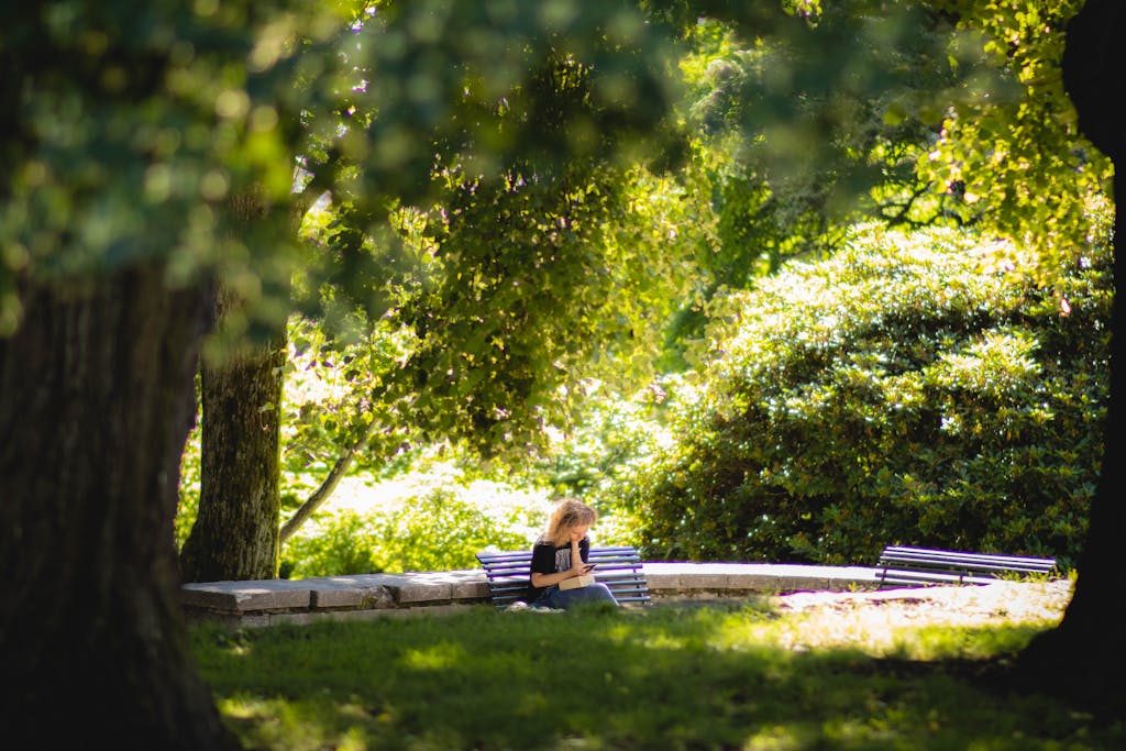 A woman reading on a bench surrounded by lush greenery in an Oslo park.